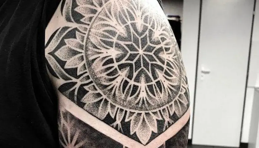 Elegancki tatuaż mandala damski na ramieniu, wykonany techniką dotwork. Wzór przypomina kwiat lub słońce.