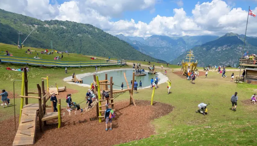 Un'area giochi con un laghetto e un galeone, dove tante famiglie si divertono in montagna con i bambini.