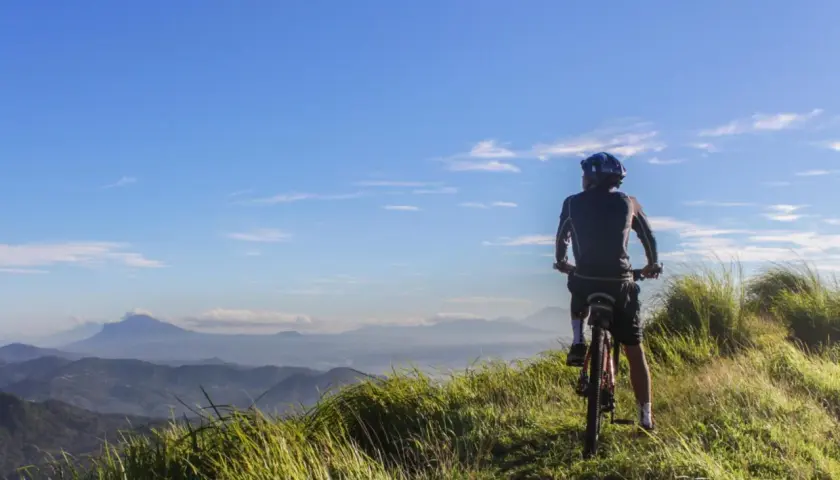 Ciclista en la cima de una colina, disfrutando de las vistas de Galicia en bici. El cielo azul y las montañas de fondo crean un paisaje impresionante.