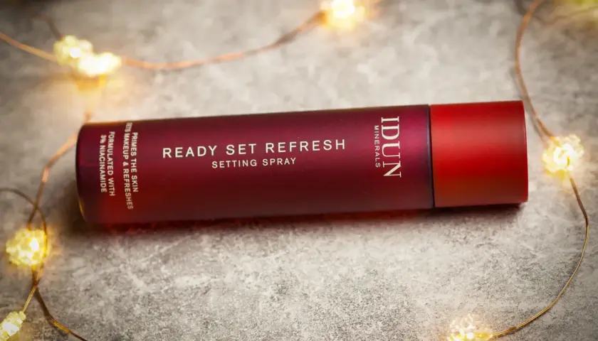 En röd flaska med IDUN Minerals Ready Set Refresh Setting Spray ligger bland julbelysning.