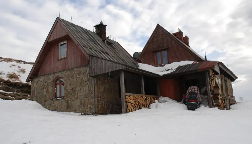 Kamienna Chatka Puchatka w Bieszczadach, zasypana śniegiem, z drewnianym zadaszeniem i stosem drewna.