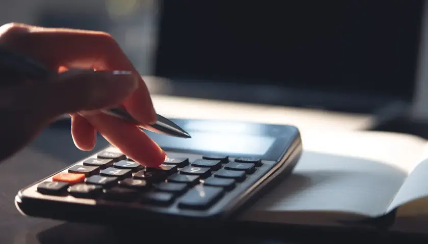 Dłoń z długopisem naciska klawisze kalkulatora, licząc, ile zarabia 1% najbogatszych Polaków. Obok leży otwarty notatnik i laptop.