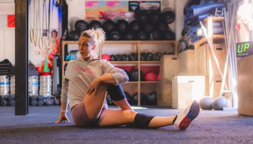 Femme en tenue de sport s'étirant au sol, profitant des bienfaits des étirements dans une salle de sport.