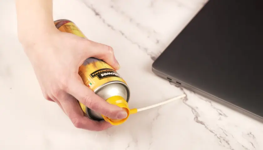 Main d'une personne utilisant une bombe d'air comprimé pour nettoyer un ordinateur portable.