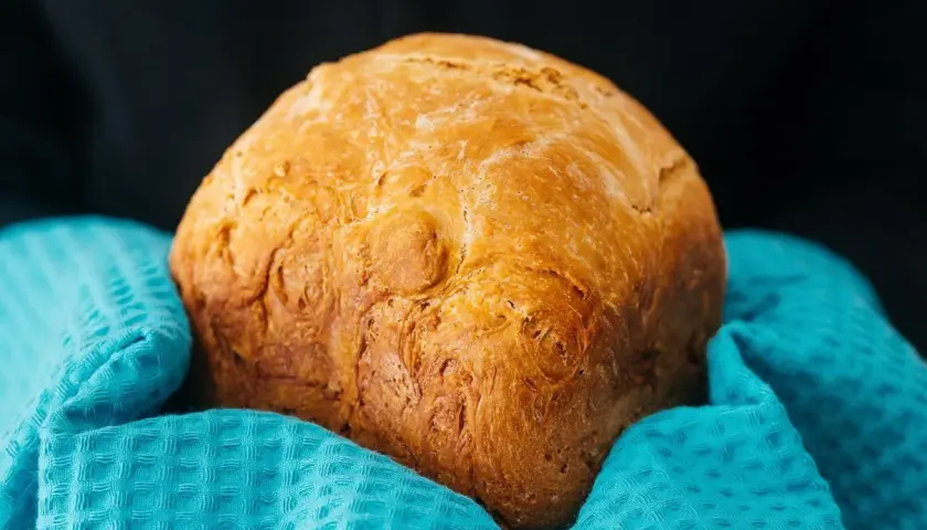 Złocisty chleb z airfryer, pachnący świeżością, otulony turkusowym ręcznikiem. Idealny na śniadanie.