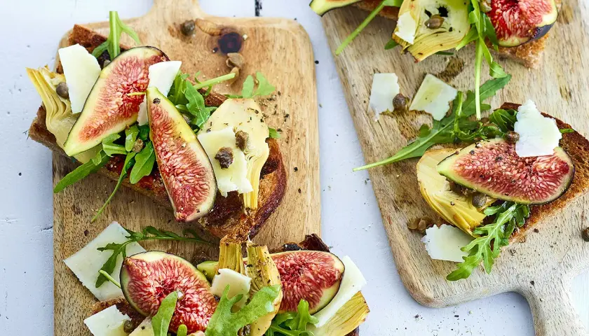 Tartines de pain grillé garnies de figues fraîches, d'artichauts, de roquette et de copeaux de parmesan.