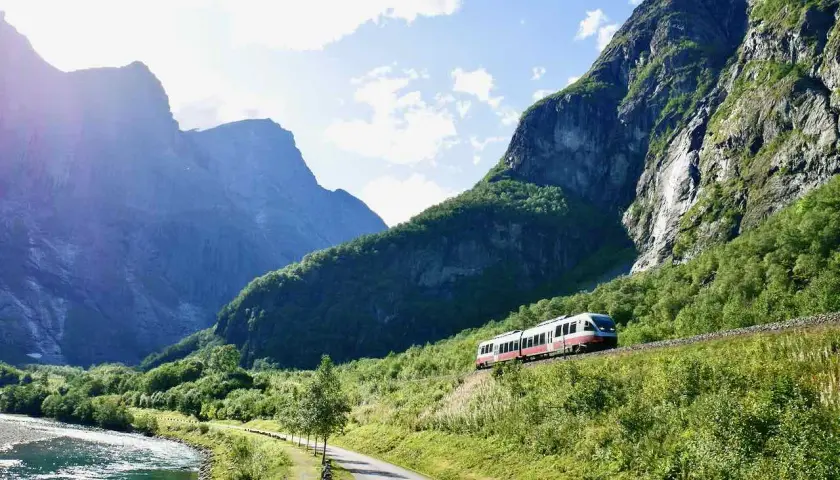 Ein Zug fährt durch eine malerische Berglandschaft. Ein perfekter Urlaub mit dem Zug, vorbei an einem Fluss und grünen Hängen.
