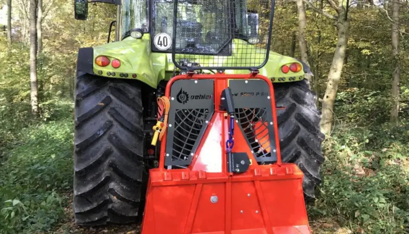 Ein grüner Traktor mit einem roten Forstkran im Wald.