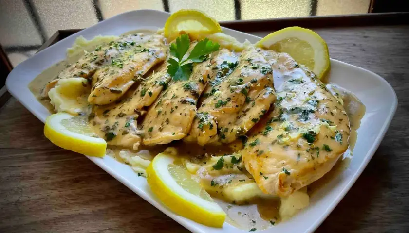 Delicioso pollo al limón con puré de patatas, adornado con rodajas de limón y perejil fresco.