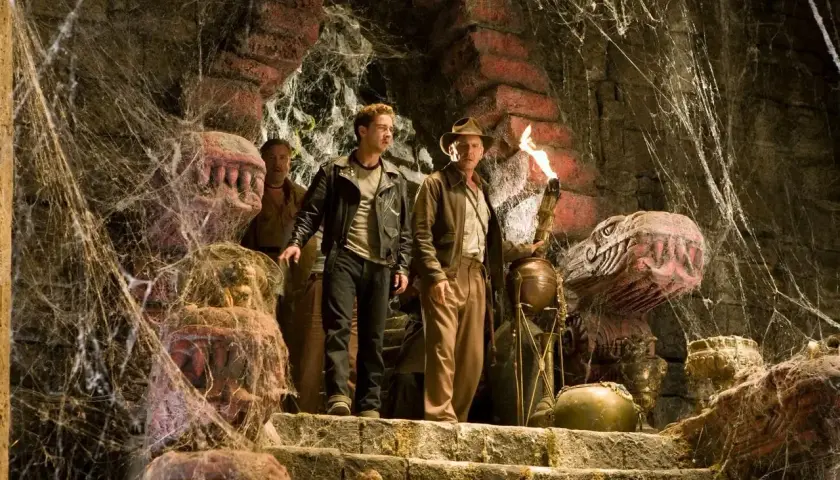 Indiana Jones i Królestwo Kryształowej Czaszki obsada: Indiana z pochodnią i Mutt na schodach w pajęczynach, obok kamiennych głów.