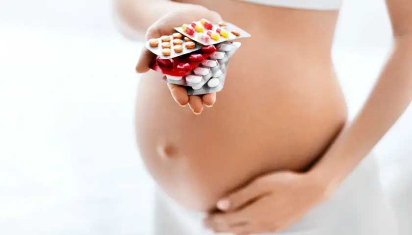 Kobieta w ciąży trzyma w dłoni opakowania leków przeciwbólowych.