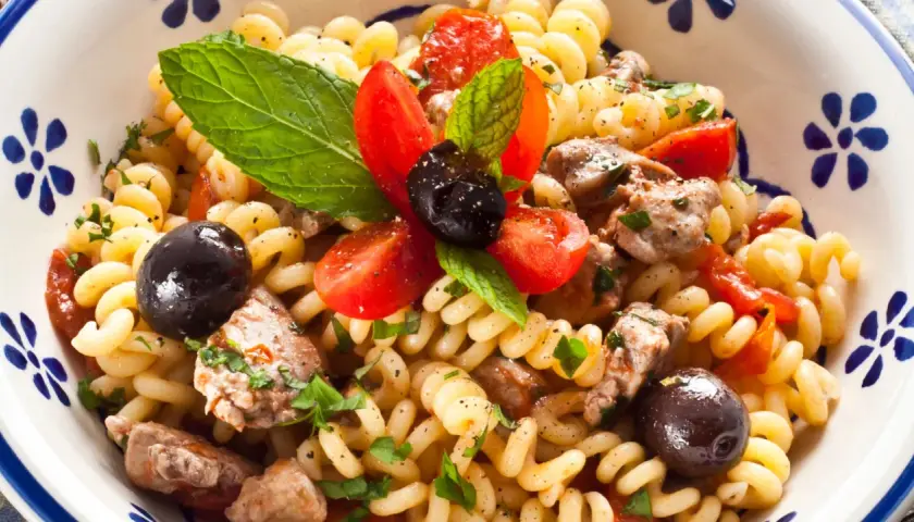 Pasta con pesce spada, pomodorini, olive nere e menta fresca in una ciotola decorata.