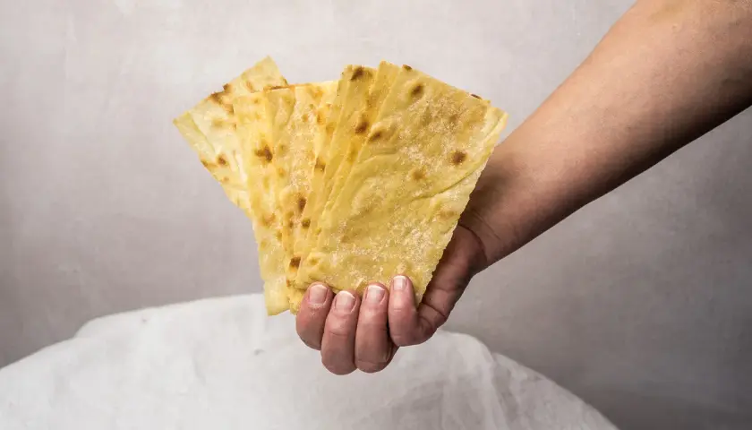 Mano sostiene varias láminas de pan carasau dorado y crujiente, con pequeñas manchas tostadas.