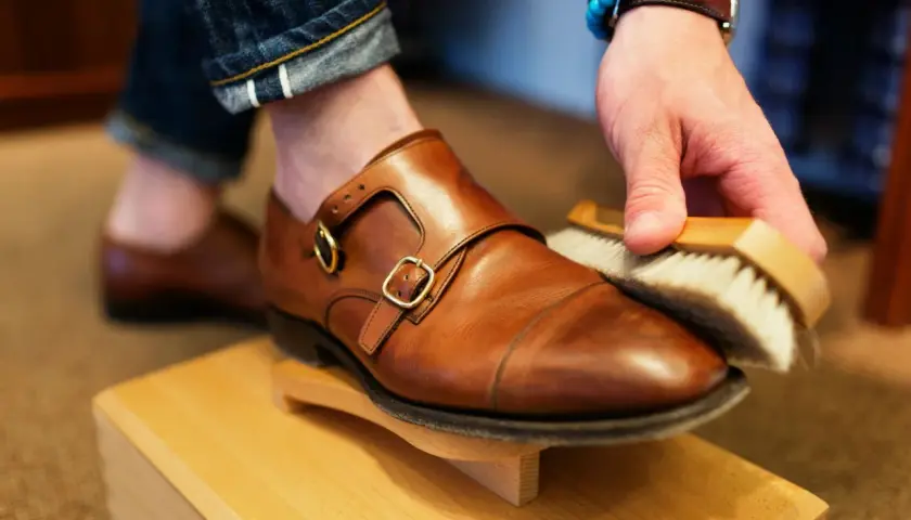 Hombre cepillando un zapato de piel marrón, parte de como limpiar zapatos de piel.