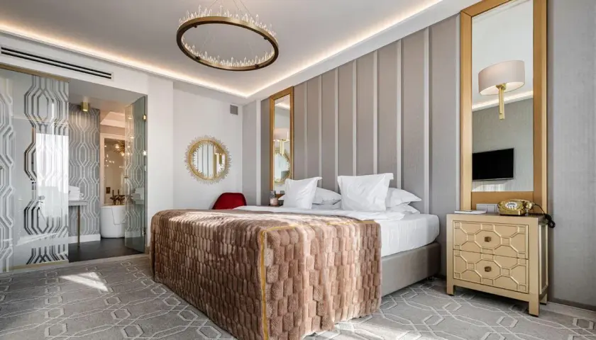 Elegancki pokój hotelowy 4-gwiazdkowy spełniający wysokie wymagania: łóżko z puszystym kocem, kryształowy żyrandol, złote lustra i stylowe meble.