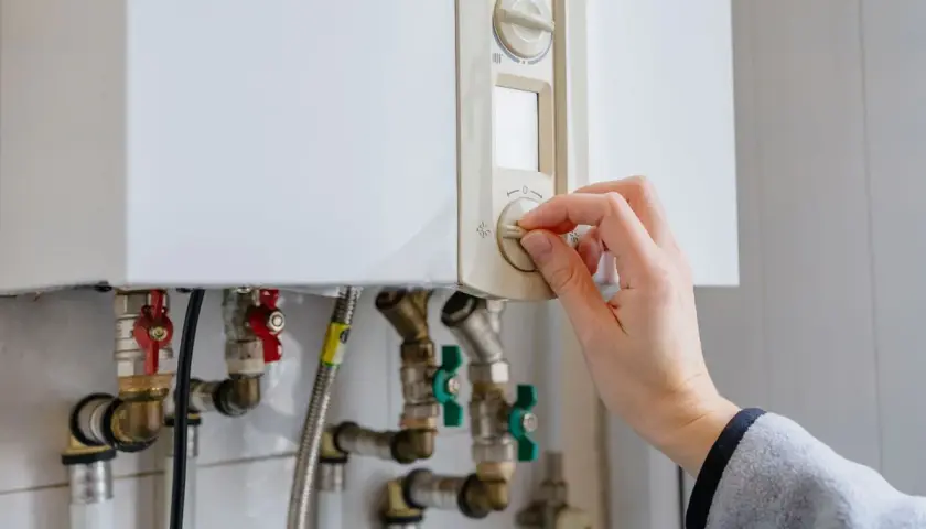 Main tenant ajuste le thermostat de sa chaudière à gaz. Une aide pour le changement de chaudière gaz est peut-être nécessaire.