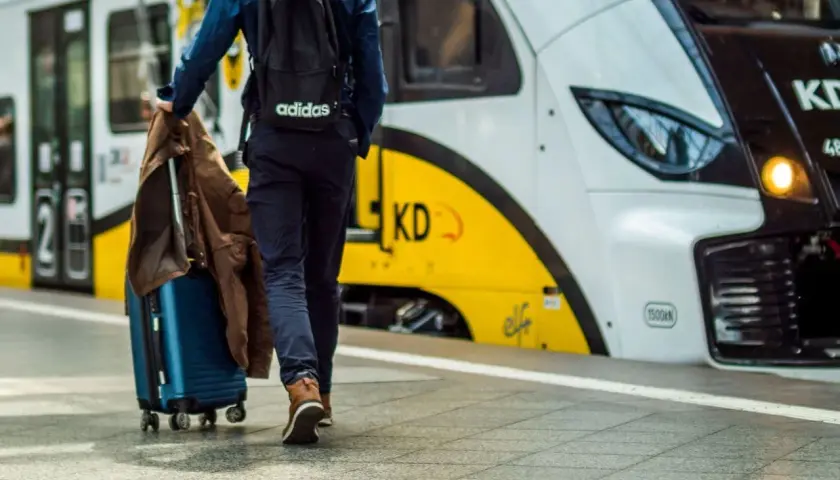 Podróżny z walizką i kurtką idzie na pociąg. Może to być podróż z Warszawy do Gdyni.
