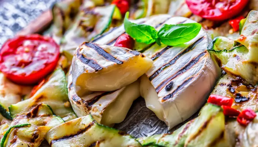 Co na grilla oprócz mięsa? Grillowany ser camembert z cukinią i pomidorami, udekorowany bazylią.