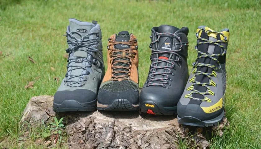 Four hiking boots, showcasing what boots are made of, sit on a log. Materials include leather, mesh, and rubber soles.