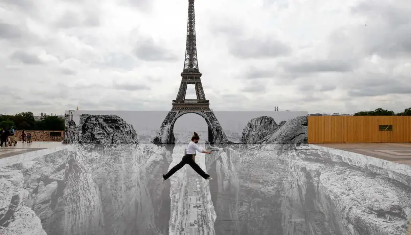 Une femme saute au-dessus d'un gouffre dessiné par un peintre trompe l'oeil connu, avec la Tour Eiffel en arrière-plan.