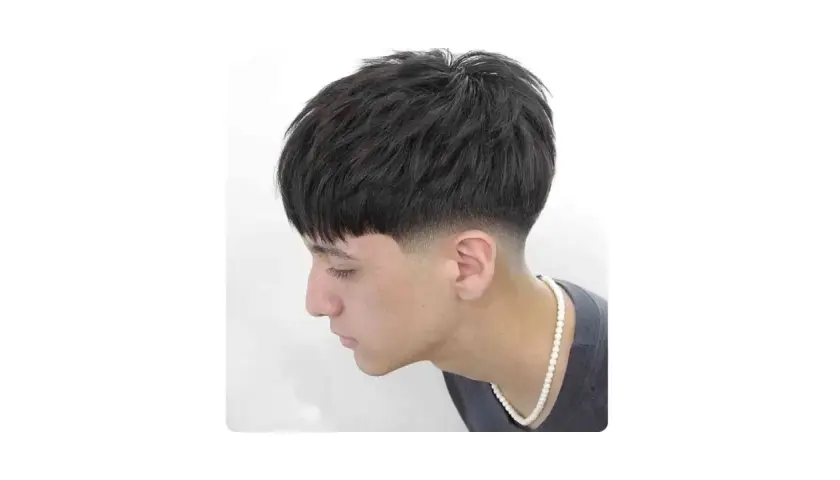 Joven con corte de pelo moderno, con flequillo recto y un degradado bajo (low fade) en los laterales.