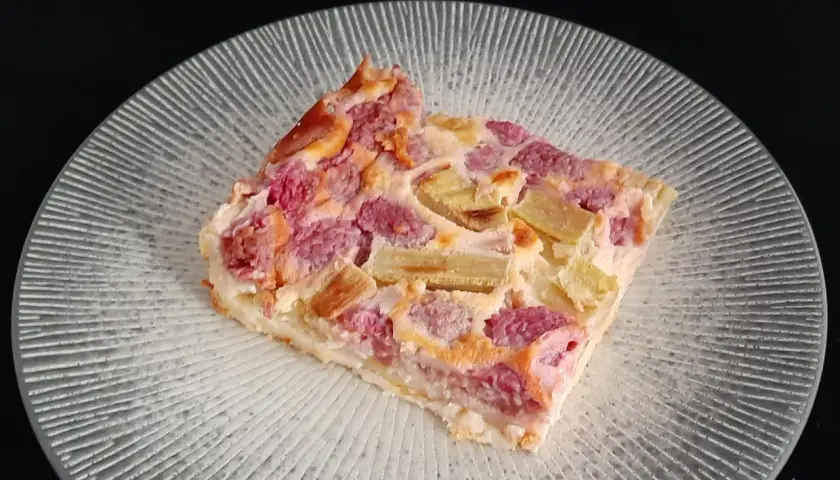 Tranche de clafoutis rhubarbe aux fruits rouges, sur une assiette transparente aux motifs rayonnants.