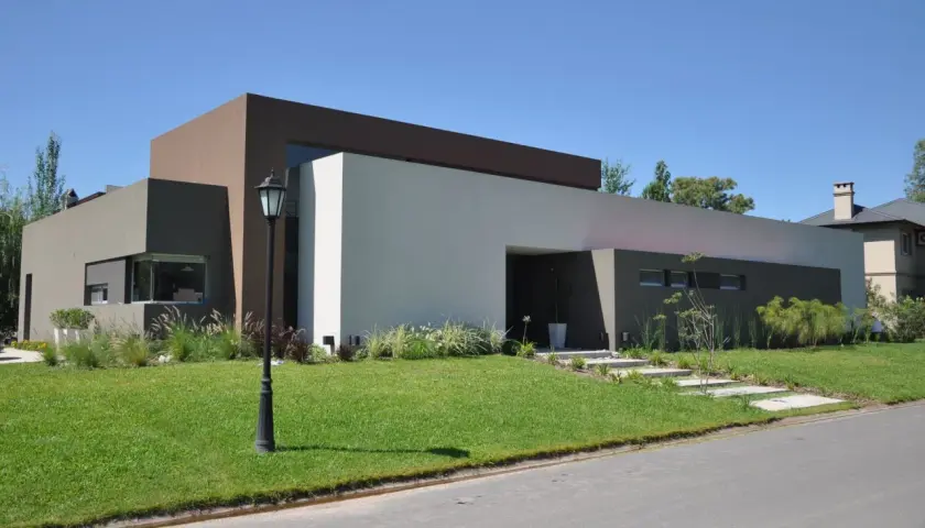Casa moderna con pintadas color de casa afuera, en tonos tierra y blanco. Jardín verde y cielo azul.
