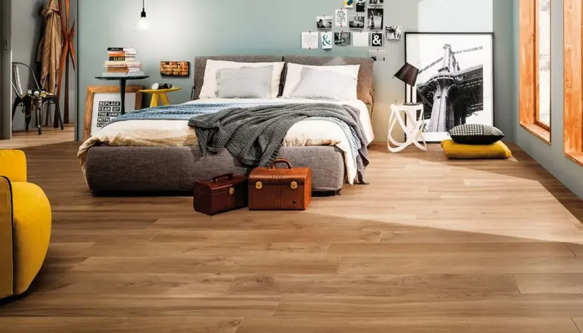Camera da letto moderna con letto grigio, poltrona gialla e pavimento in **gres porcellanato** effetto legno.