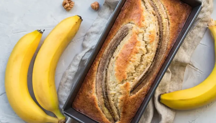 Gâteau moelleux à la banane trop mûre, cuit à la poêle, avec des bananes fraîches et des noix autour.
