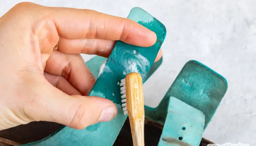 Hand reinigt türkisfarbene Birkenstock-Riemen mit einer kleinen Bürste und Seife. So einfach ist das Birkenstock reinigen!