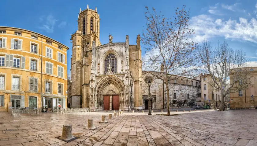 Katedra w Aix-en-Provence, z żółtą kamienicą obok, na brukowanym placu pod błękitnym niebem.