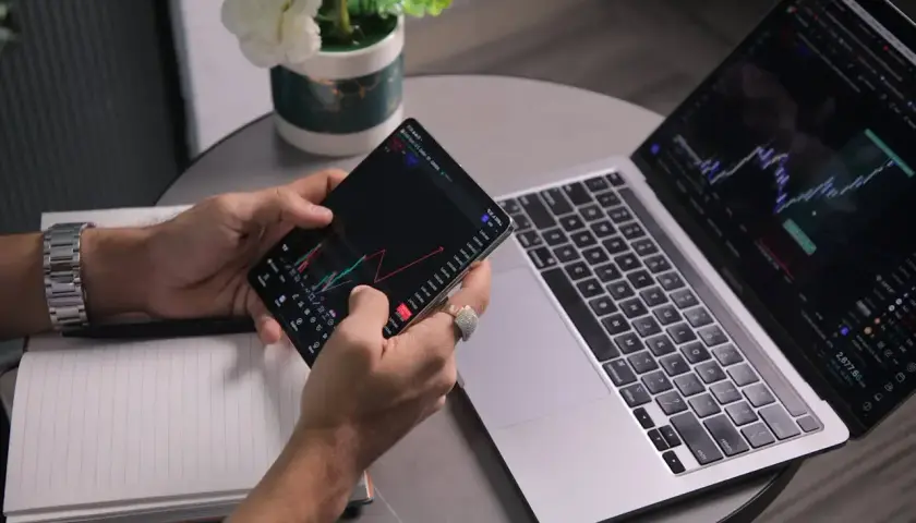 Analityk sprawdza wykresy na telefonie i laptopie, analizując dane finansowe.