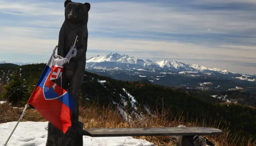 Drewniany niedźwiedź z flagą Słowacji na szczycie Veterny Vrch, z widokiem na ośnieżone Tatry.