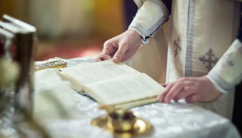 Dłoń duchownego trzyma księgę, czytając tekst. To może być fragment o tym, czym jest rezurekcja.