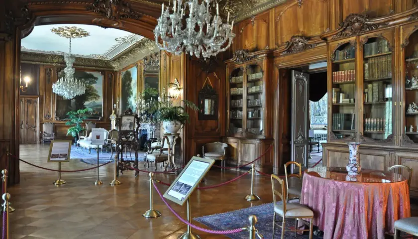 Eleganckie wnętrza Zamku w Pszczynie: kryształowe żyrandole, bogato zdobione boazerie, zabytkowe meble i biblioteka.