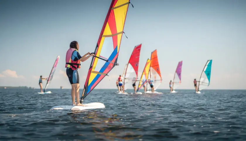 Ludzie na deskach z żaglami, uczący się, co to windsurfing. Wesoła grupa na wodzie w słoneczny dzień.