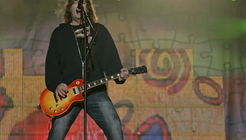 Wokalista z gitarą na scenie, podczas koncertu. Analiza piosenki "Kocham Cię Jak Irlandię" mogłaby opierać się na tej emocjonalnej chwili.