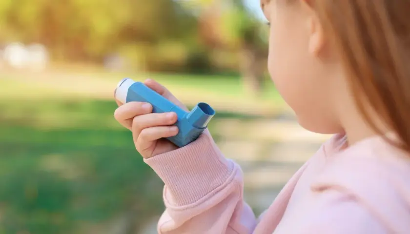 Bambina con inalatore blu, per gestire la tosse asmatica e i suoi sintomi.