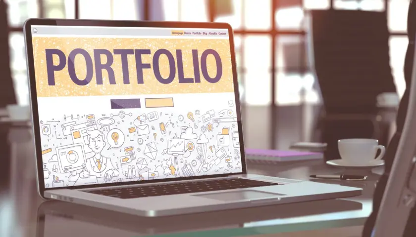 Laptop z napisem "PORTFOLIO" i rysunkami symbolizującymi pracę kreatywną. To świetny przykład, portfolio co to jest.