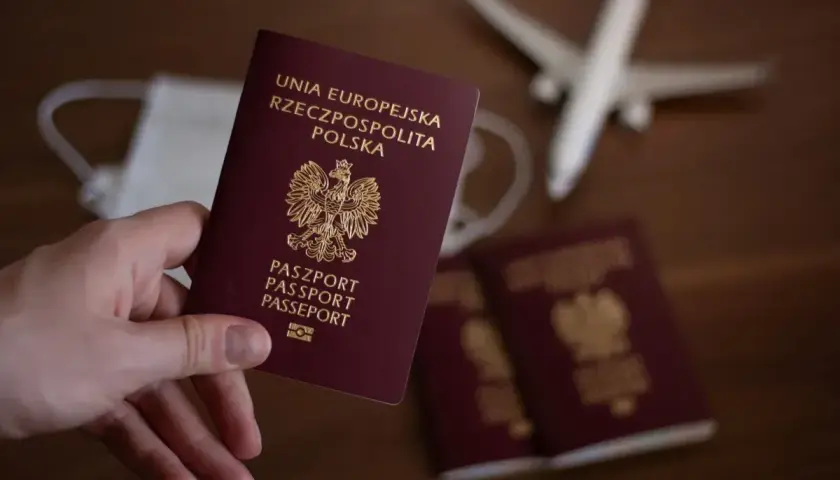 Dłoń trzyma polski paszport. Obok leżą kolejne paszporty, maseczka i samolot. Czas na podróż, ale ile wyrabia się paszport?