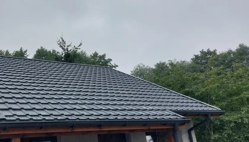 Szary dach z blachy, idealny przykład, jak uszczelnić dach przed deszczem. Wokół zielone drzewa.