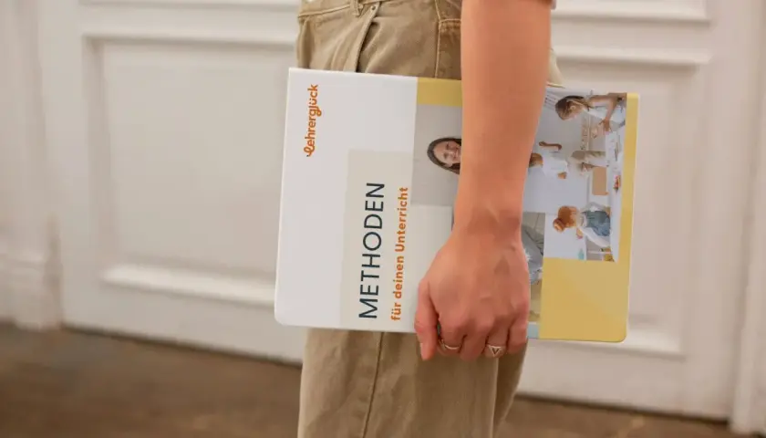 Ein Buch mit dem Titel "Methoden für deinen Unterricht" wird von einer Person gehalten. Es zeigt Bilder von Kindern in einer Lernumgebung.