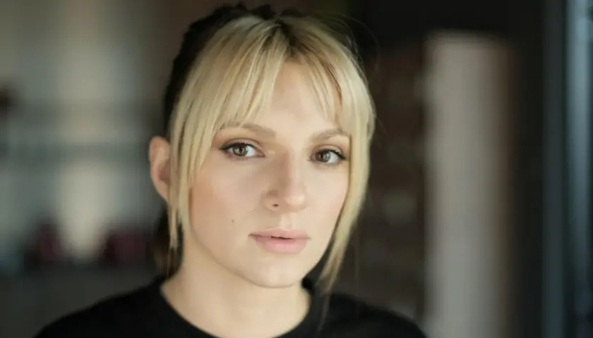 Portret młodej kobiety z blond grzywką i ciemnymi pasemkami włosów, patrzącej w obiektyw.