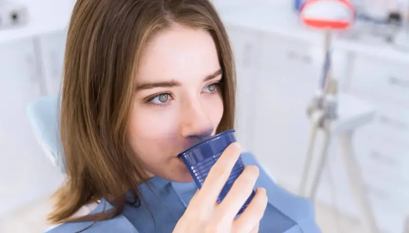 Ragazza in poltrona dentistica beve da un bicchierino blu, forse dopo un trattamento con clorexidina cos'è.