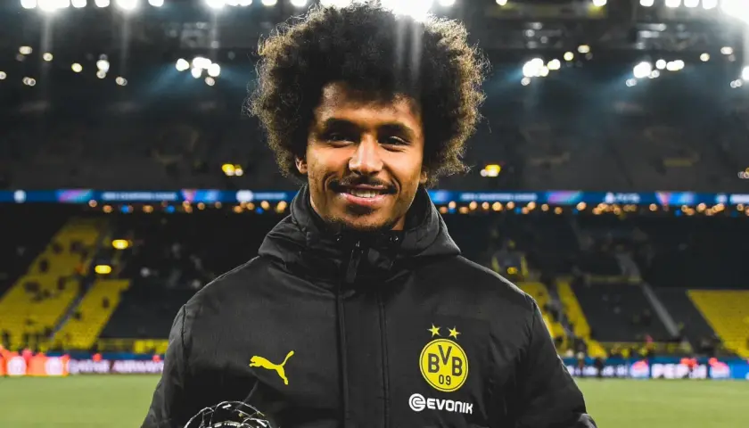 Karim Adeyemi z BVB z pucharem, uśmiecha się na tle stadionu.
