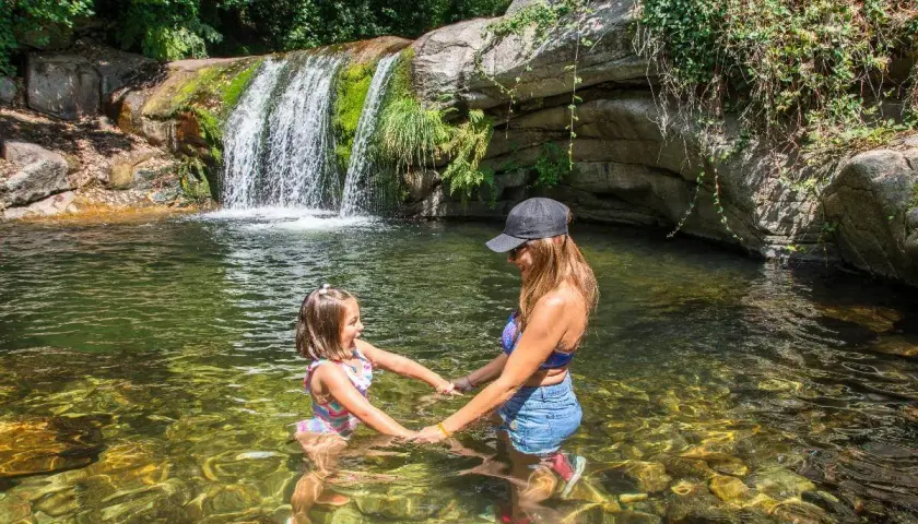 Madre e hija disfrutan de unas refrescantes piscinas naturales con una cascada al fondo.