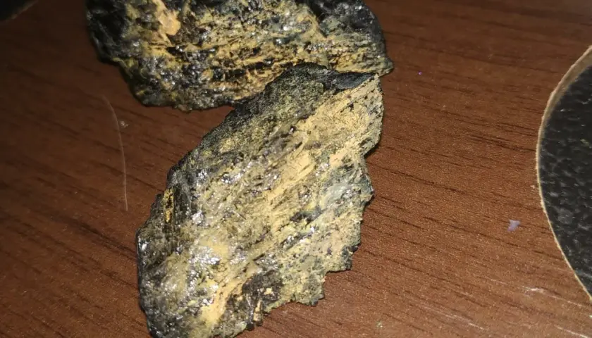Dwa kawałki czarnego turmalinu, które pękły, pokryte żółtym nalotem, leżą na drewnianym blacie.