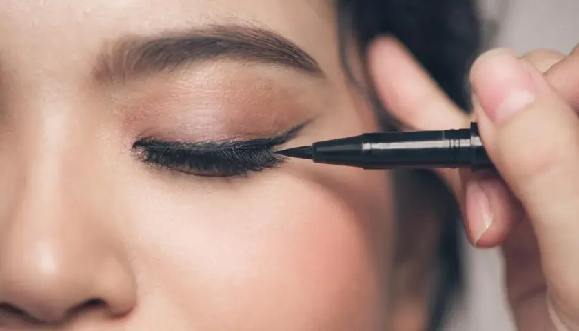 Precyzyjne malowanie odwrócone kocie oko makijaż. Czarny eyeliner podkreśla spojrzenie.