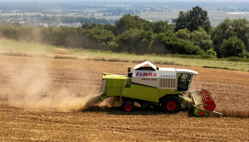 Kombajn zbożowy CLAAS Mega 350 zbiera plony na polu. Dymiące maszyny rolnicze to symbol ciężkiej pracy, która dzięki płatnościom bezpośrednim staje się bardziej opłacalna.