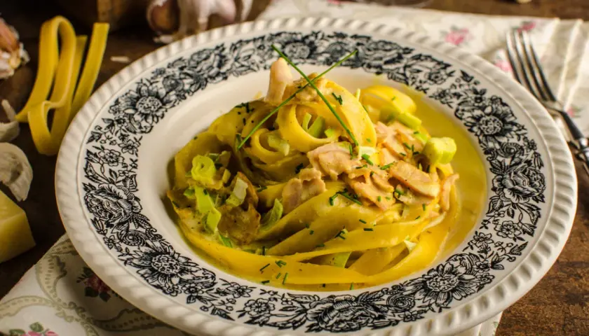Talerz z makaronem tagliatelle w kremowym sosie z kawałkami mięsa i szczypiorkiem.
